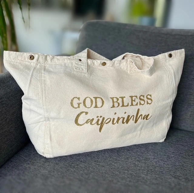 Sac fourre-tout blanc avec "God bless Caïpirinha" en or pailleté.