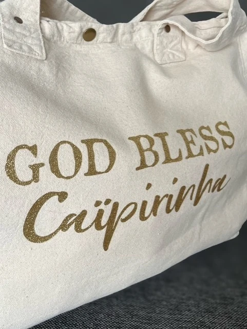 Sac fourre-tout blanc avec "God bless Caïpirinha" en or pailleté.