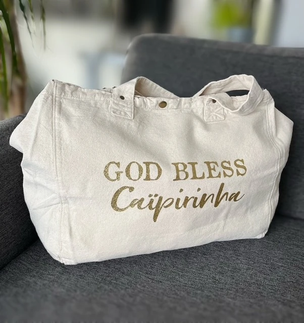 Sac fourre-tout blanc avec "God bless Caïpirinha" en or pailleté.