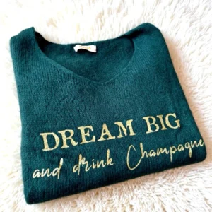 Pull femme en baby alpaga vert bouteille, slogan "Dream big and drink Champagne" en or pailleté. Col V. Slogan iconique signé La Strasseuse.