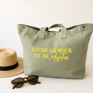 Sac cabas vert sauge « Vivre d’amour et de Mojitos » avec flocage jaune fluo, présenté sur un fond clair avec chapeau de paille et lunettes de soleil.