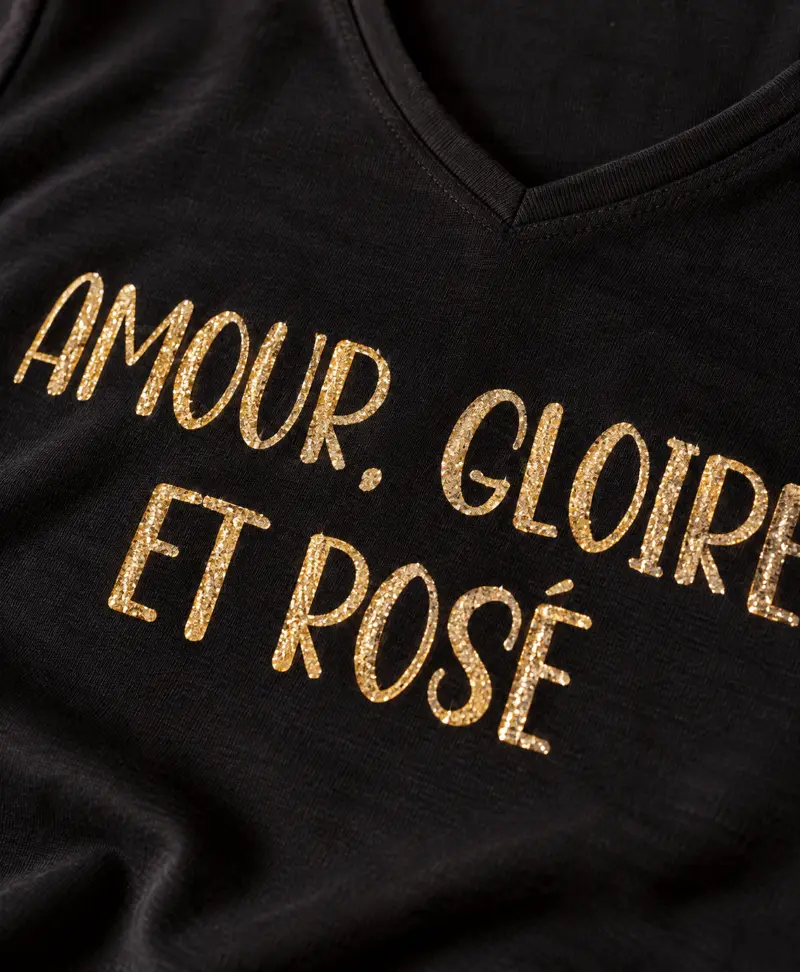 Gros plan du flocage doré pailleté "Amour, Gloire et Rosé" sur tee-shirt en coton noir.