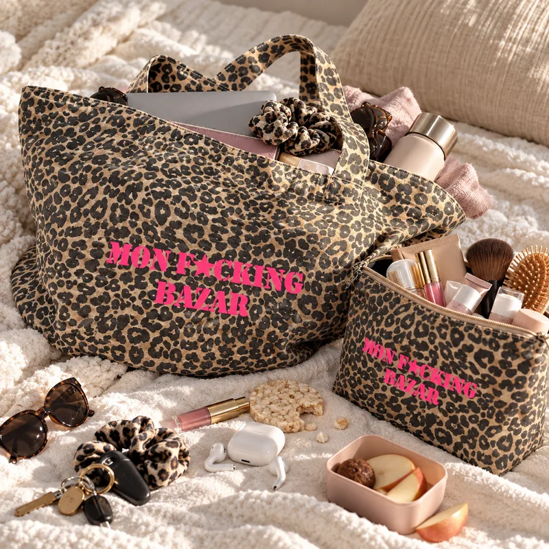 Duo léopard Mon F*cking Bazar rose fluo sur un plaid crème, tote rempli et trousse ouverte pleine de maquillage, entourés de clés, écouteurs et goûter