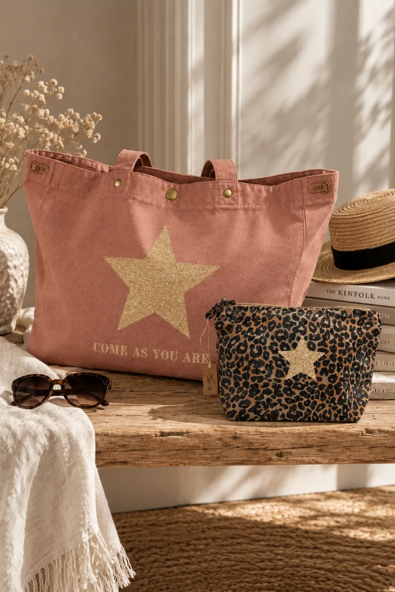 Sac cabas XXL santal « Come As You Are » à étoile or pailletée et trousse de toilette léopard à étoile champagne pailletée, posés sur un banc en bois. Création La Strasseuse.