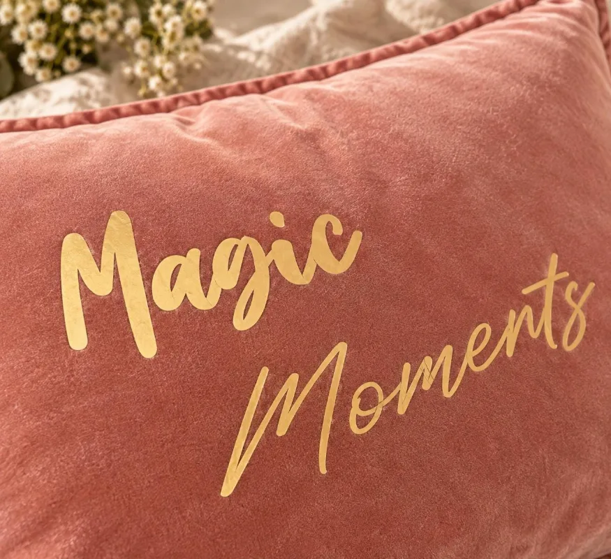 Gros plan sur la texture du velours de coton vieux rose et le slogan Magic Moments en lettres dorées mates de la housse de coussin.