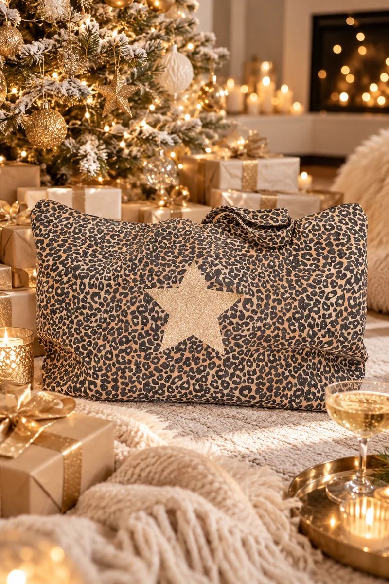 Maxi tote bag léopard étoile champagne pailletée posé au pied d'un sapin de Noël doré, entouré de paquets cadeaux, de bougies et d'une coupe de champagne
