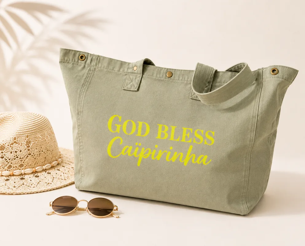 Sac fourre-tout vert sauge avec "God bless Caïpirinha" en jaune fluo, sur fond clair avec chapeau en crochet et lunettes de soleil. Création La Strasseuse.