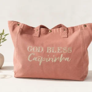 Sac fourre-tout vieux rose avec "God bless Caïpirinha" en or pailleté, sur une table claire avec une branche d'olivier. Création La Strasseuse.