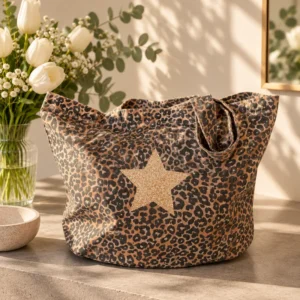 Tote bag léopard XL avec une grande étoile champagne pailletée, posé sur une console à côté d'un bouquet de tulipes blanches